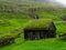 Saksun. Wooden old house with grass roof. Green fields, waterfall over the village. Hazy landscape. Clouds over the