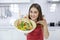 Salad in a bowl shown by Asian women in the kitchen. Woman in kitchen with various kind of vegetable