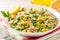 Salad with bulgur, green peas, corn, onion and greens on white rustic wooden table. Tabbouleh.