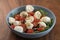 Salad with mozxarella, tomatoes and arugula in a blue bowl on walnut wood table