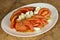 Salad with peeled tomatoes. In a white plate on a wooden background.