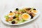 Salad with salmon, eggs and olives on white dish