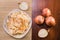 Salad of sauerkraut and carrots in a white plate and several onion bulbs on a wooden table