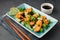 Salad with shrimp, pineapple and fresh herbs in a blue plate on a black background.