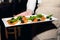 Salad of tomatoes basil and basil olives on a white rectangular plate in the hands of the waiter close up