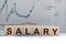 Salary text written on wooden block with stacked coins on grey background