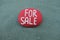 For Sale, handmade red stone sign on a stone over green sand