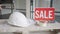 Sale sign in empty premises with Caucasian hand hitting hammer on hard hat. Office or house for sale indoors. Repair