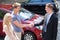 Salesman and couple shaking hands by car