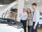 A salesman demonstrates a car with an open hood to an elderly Caucasian couple in a car dealership.