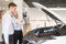 A salesman demonstrates a car with an open hood to an elderly Caucasian couple in a car dealership.