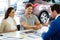 Salesman giving the key of the new car to a young couple at the dealership showroom