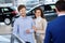 Salesman talking to a young couple at the dealership showroom.