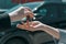 Salesperson hand giving keychain to a female client at the showroom with modern black car on the background