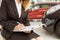 Saleswoman sitting near cars while writing on clipboard