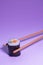 Salmon and avocado maki being caught with chospticks on purple background. Japanse cuisine. Vertical picture. Conceptual. Copy