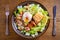Salmon caesar salad. Crispy pan fried salmon fillet, bacon, poached egg, romaine lettuce and croutons in bowl on wooden table