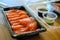 Salmon sashimi on a black plastic tray The side has soy sauce and wasabi. Is a delivery set meal