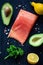 Salmon steak, avocados, lemons, parsley and spices on wooden cutting board