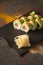 Salmon Sushi roll with avocado, red caviar on black plate, spices on dark background