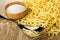 Salt in bowl, spoon, heap of egg noodles on wooden table