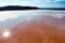 Salt lake of natural pink and orange color with salt accumulations near the shore. The sun is reflected on the water.