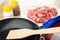 Salt and pepper, pieces of raw pork meat in plate, spatula in frying pan on table