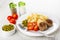 Salt and pepper, tomato, bowl with green peas, plate with cooked pasta, fried patties, green peas, tomato, fork on wooden table