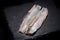 Salted boneless fillets of wild-caught Atlantic Herring arranged on natural black stone. Clupea harengus.