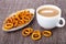 Salted bread rings in oblong plate, cup of cocoa with milk, scattered rings on mat