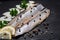 Salted Deboned Herring Fillets garnished with Yellow Onion, Lemon, Fresh Parsley and Peppercorns. Natural black stone .