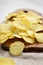 Salted wavy potato chips on a rustic wooden board on a white wooden surface, side view