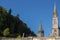 Sanctuary of Our Lady in Lourdes, France. Famous religious centre of pilgrims. Aerial view of catholic cathedral with mountains.