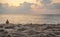 Sand on beach, closeup low angle detail, person seen from behind in background ready for morning swim, orange pink sunrise sky