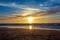 Sand beach with endless horizon and foamy waves under the bright sundown with yellow colors and clouds above the sea