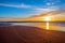 Sand beach with endless horizon and foamy waves under the bright sundown with yellow colors and clouds above the sea