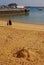 Sand bear sculpture on beach with concrete pier & fred olsen express ferry, Corralejo marina port harbour at Fuerteventura, Spain