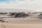 Sand dunes with dry plants, mountains and cloudy sky on background