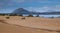 Sand dunes and wild bushes and a mountain on the background.