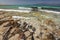 Sand on large rocks, crystal clear turquoise sea with white wave