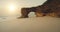 Sand ocean beach at sun light with cliff shore aerial view. Giant hole at rock wall, green grass top