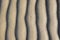Sand texture. Background with beige fine sand. Sharp lines of waves on sand. Sand surface on the beach, view from above.