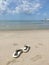 Sandals that can be taken off at the beach Green sea Blue sky and white clouds In the sun during the day.