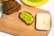 Sandwich with avocado, cream cheese and spices. A white table with a wooden cutting Board, sliced bread, toast, and a plate of