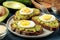 Sandwich with avocado puree and egg on a plate and ingredients for cooking on a blue wooden table