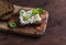 Sandwich with soft cheese, olive oil and basil, served on olive cutting board on dark wooden surface.