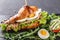 Sandwich with tuna, eggs, avocado, fresh arugula and greens on black shale board over black stone background. Healthy food concept