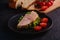 Sandwich with turkey ham meat, green salad and fresh cherry tomatoes slices on black plate near to ingredients on cutting board