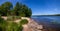 Sandy beach with large cobblestones, stones on the banks of the beautiful wide blue river Narva under the blue summer sky