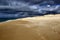 Sandy beach and navy blue ocean beneath the dark cloudy sky